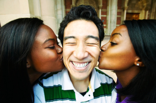 A photo of a young man being kissed on his cheeks from either side by two young women.